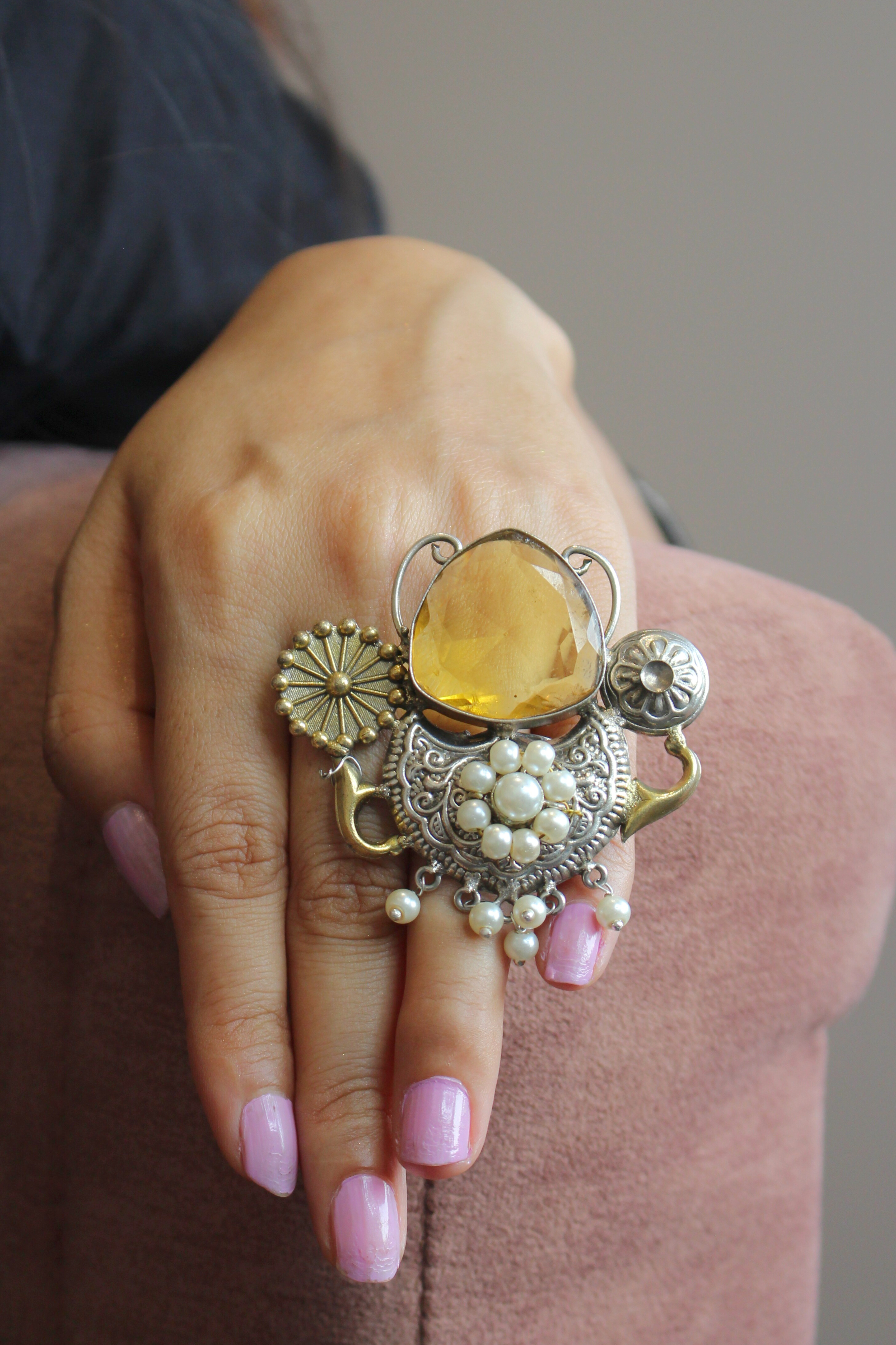 Close-up of a hand wearing an ornate ring with a yellow gemstone and pearl details.