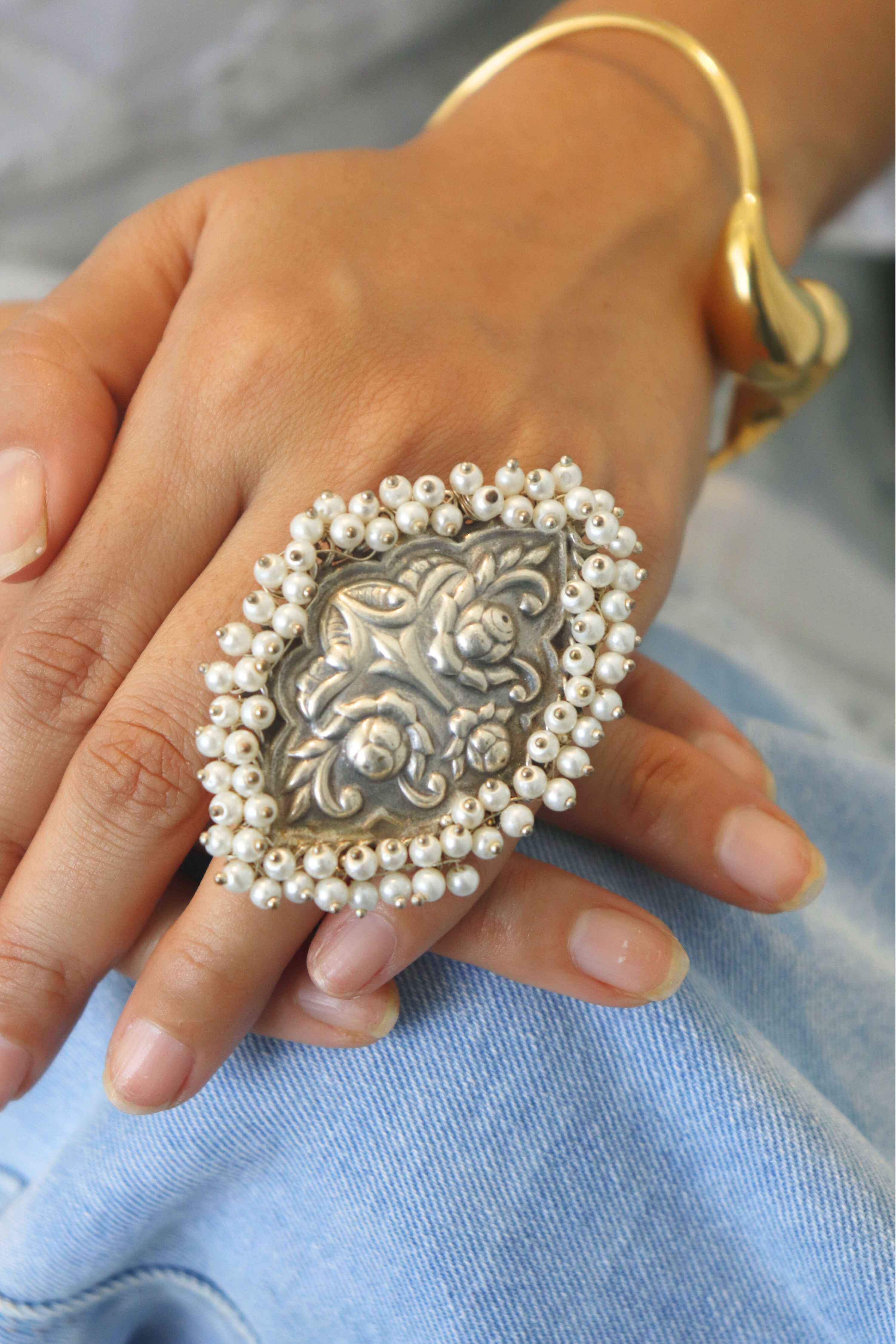 Decorative ring with pearls on a hand wearing a gold bracelet.