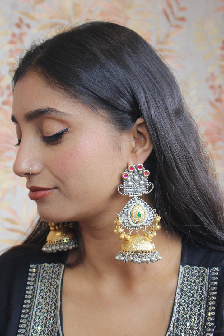 Woman wearing large, ornate silver earrings with a floral background