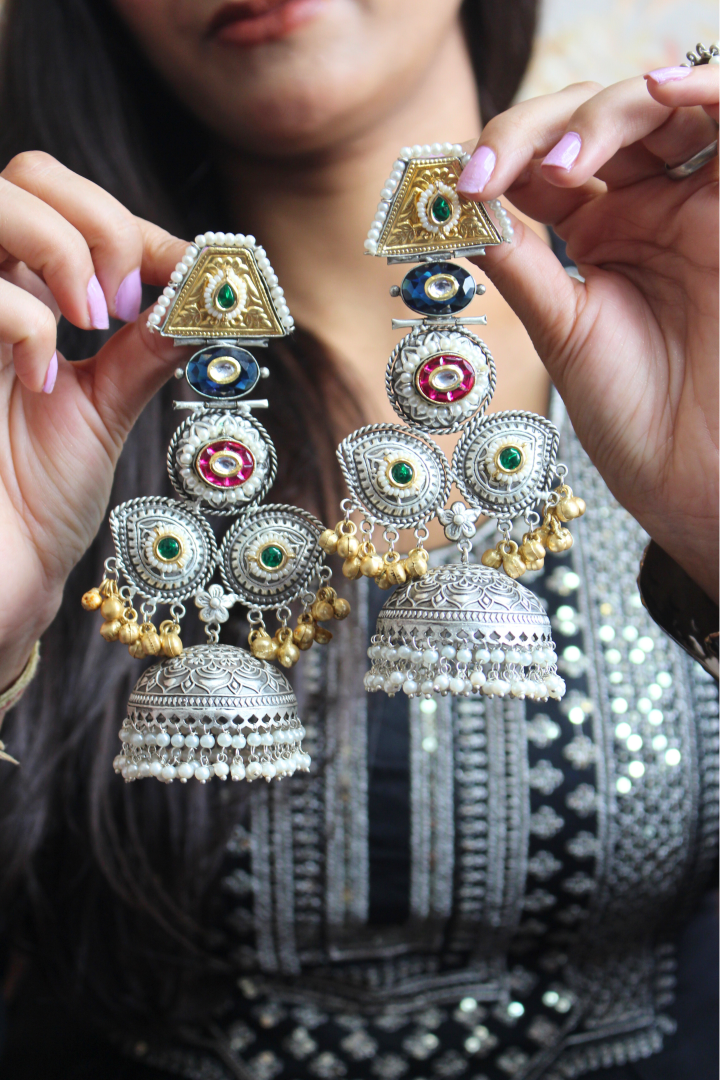 Person holding ornate silver earrings with colorful gemstones.