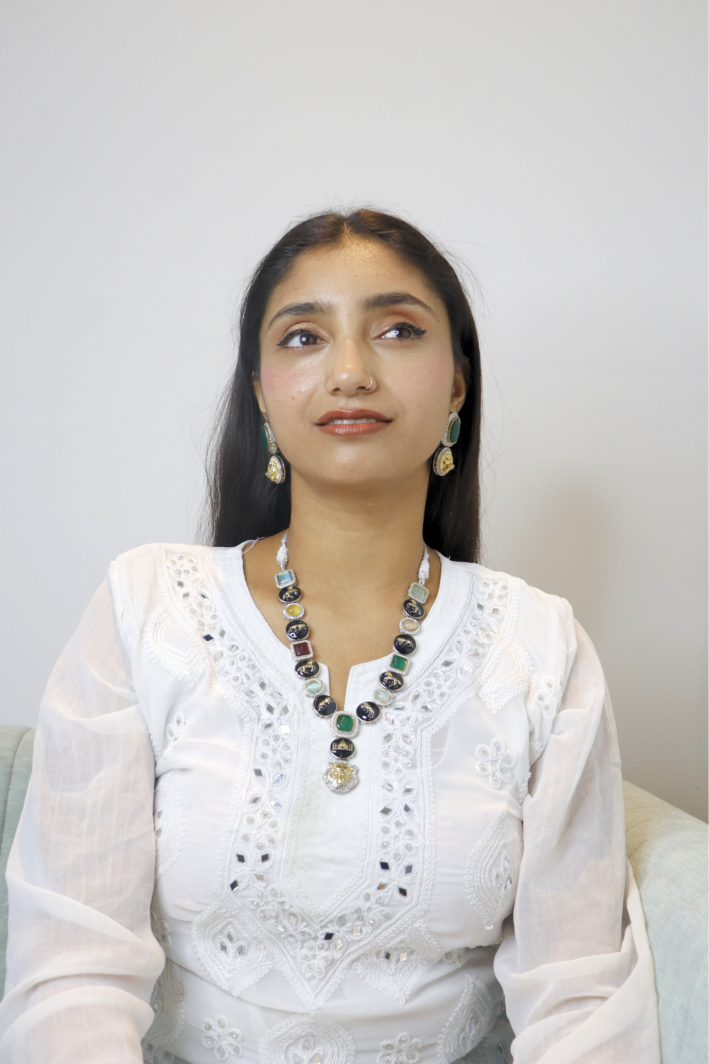 Woman wearing a white traditional outfit with a long necklace against a plain background