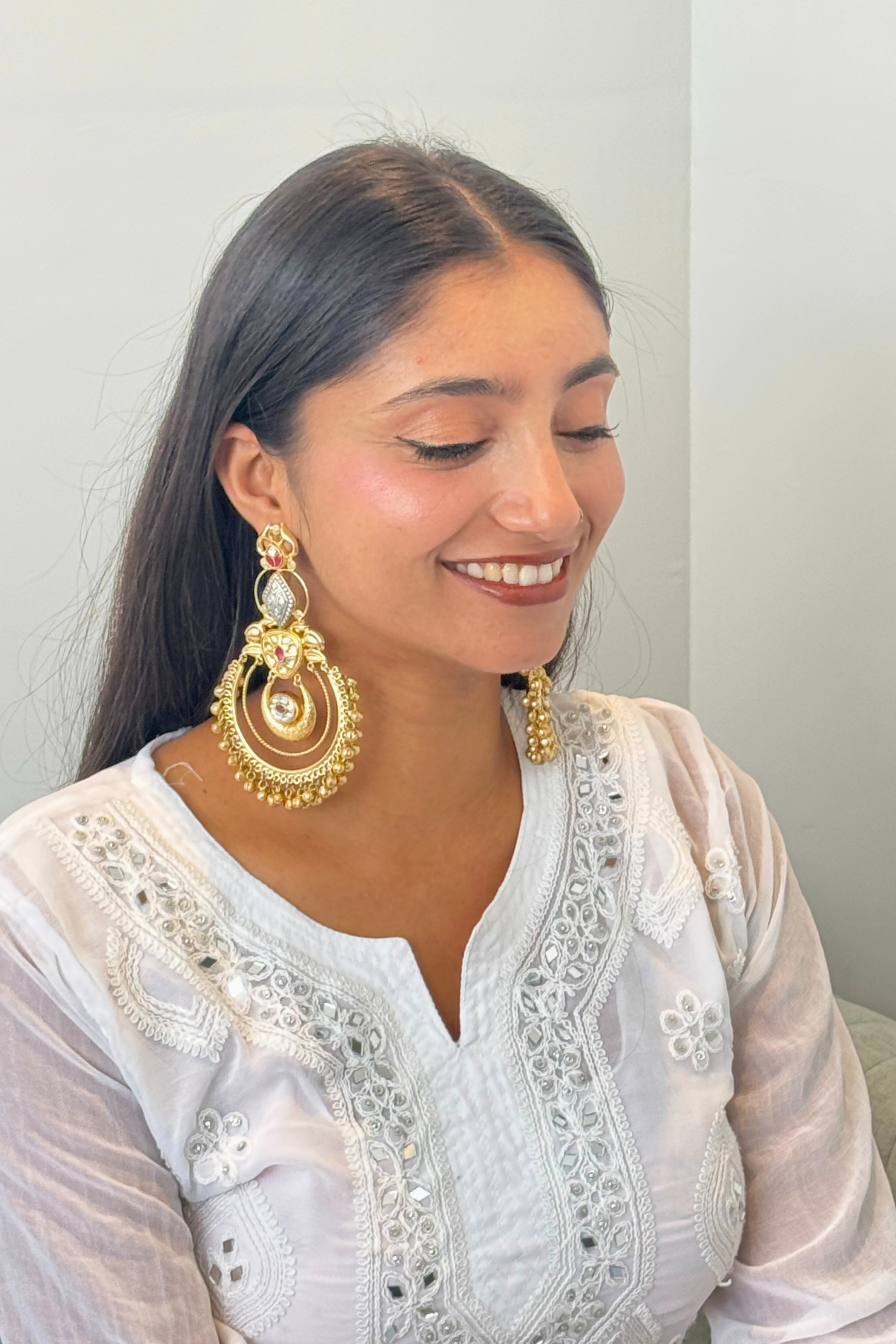 Woman wearing gold earrings and a white embroidered outfit