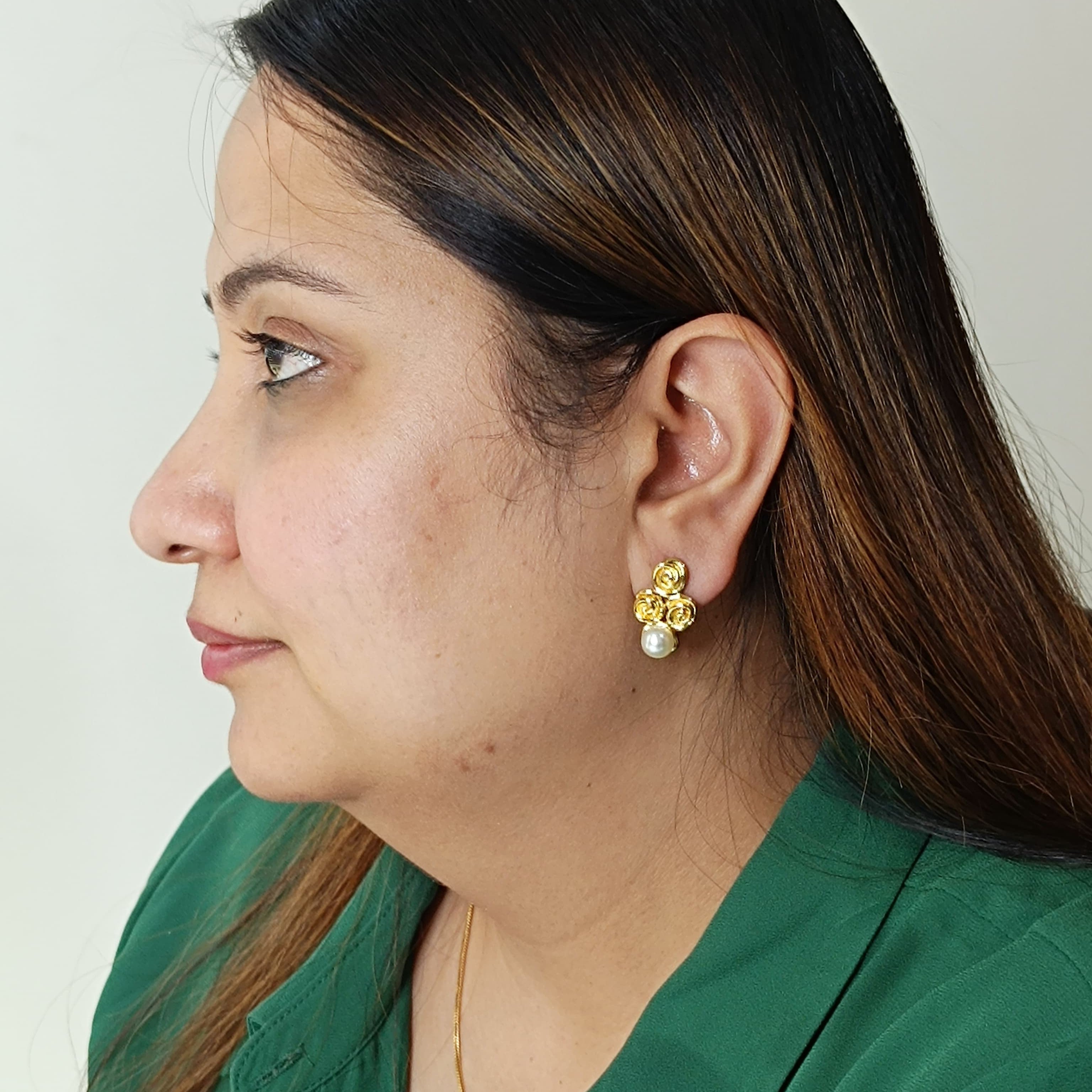 Woman wearing gold earrings with a pearl detail on a plain background