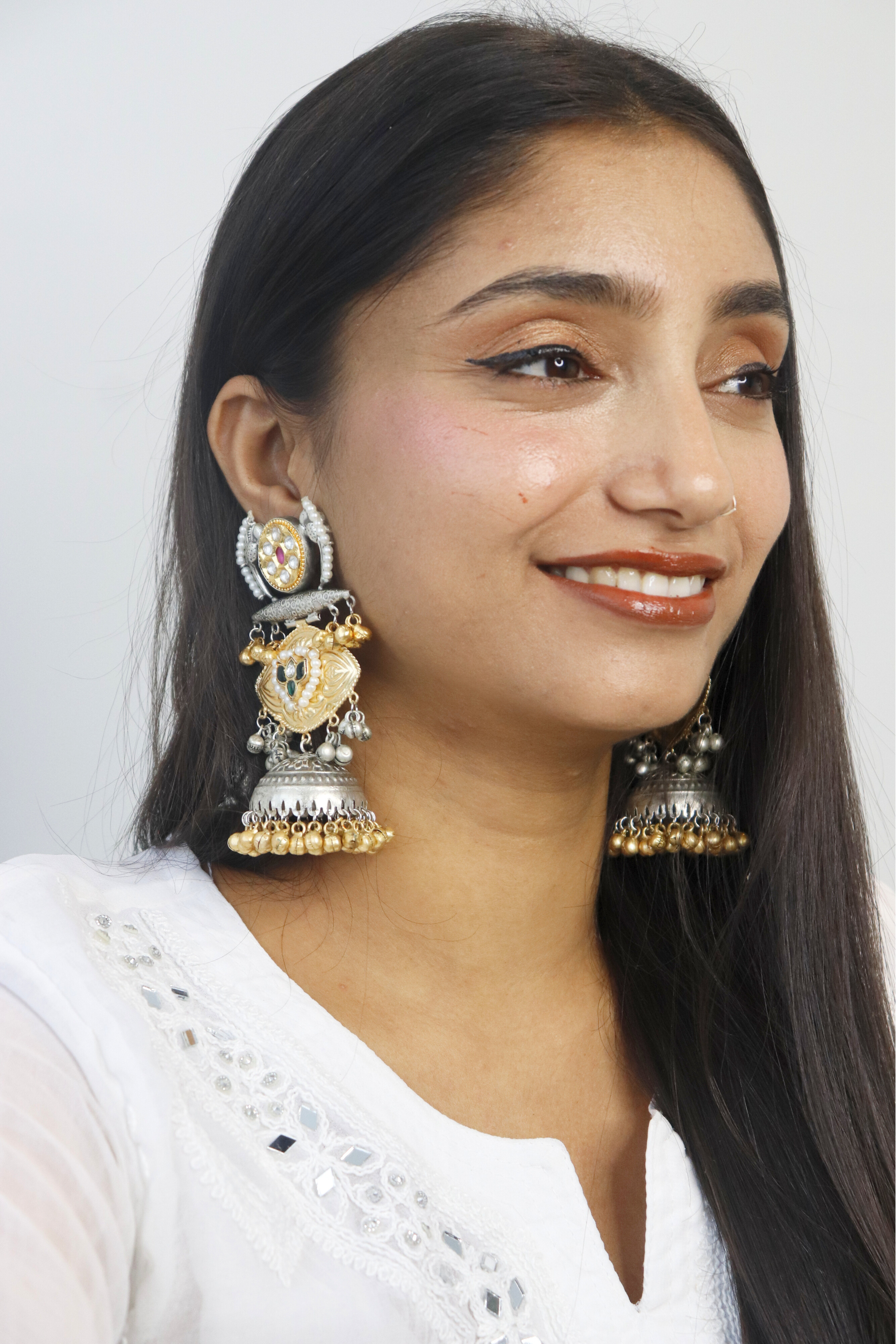 Woman wearing large, ornate earrings against a plain background