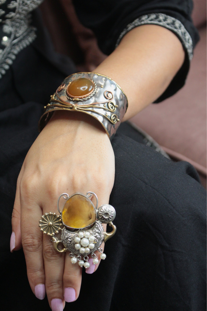 Close-up of a hand wearing a silver bracelet and ring with amber stones.