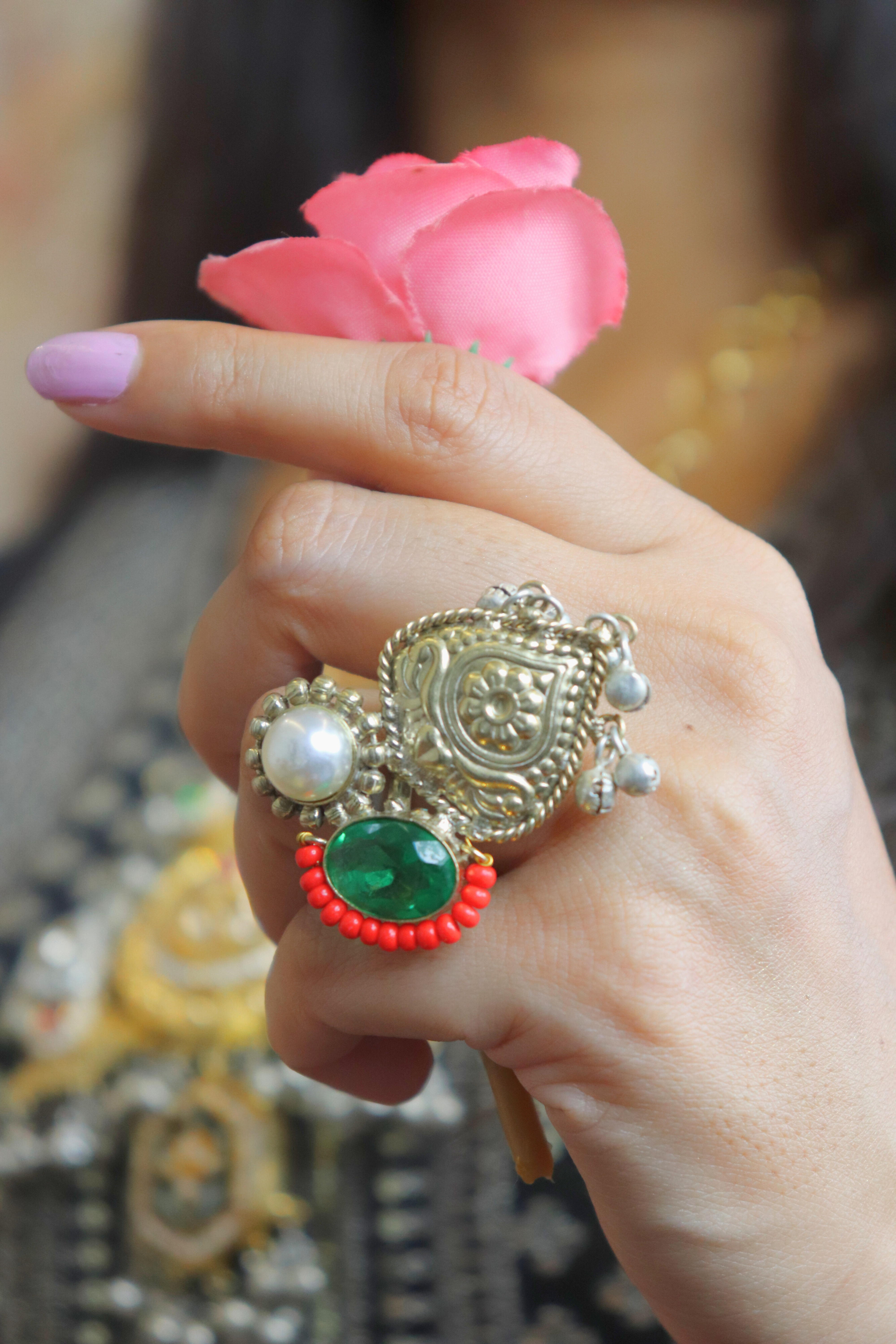 women wearing a decorative ring with a green gemstone and pink flower in the background