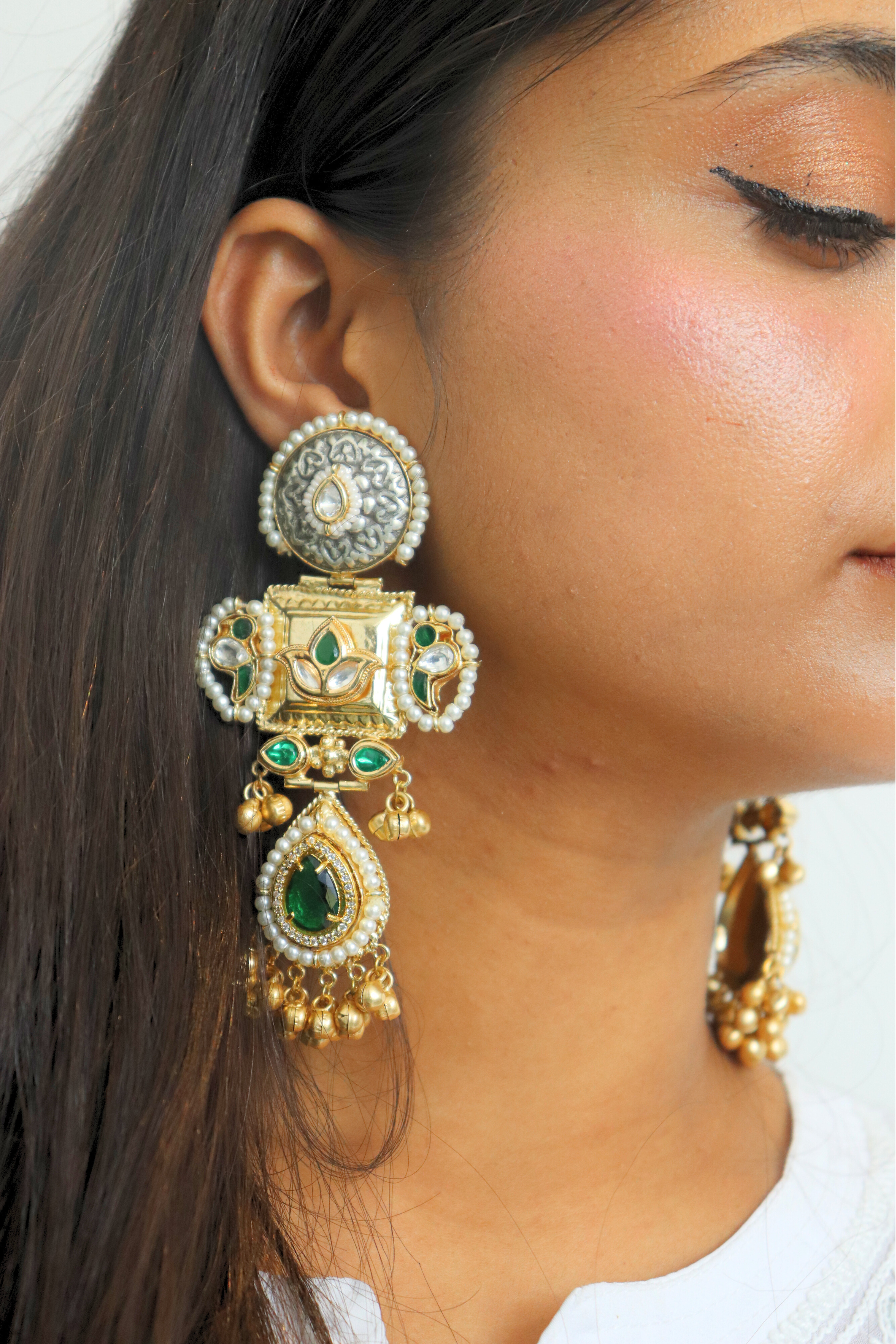 Close-up of a woman wearing ornate gold earrings with green gemstones.