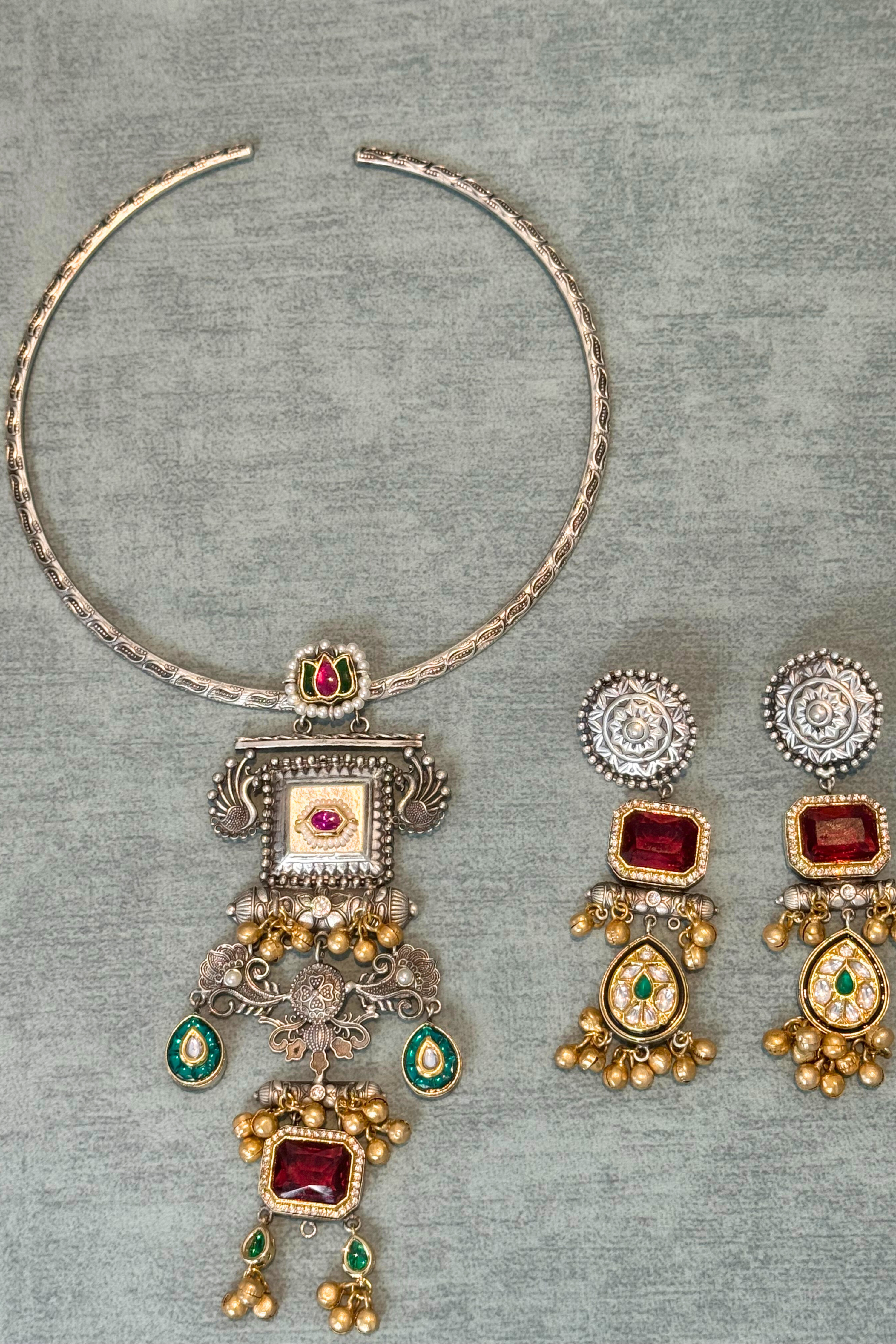 Silver necklace with red and green gemstones on a gray textured background