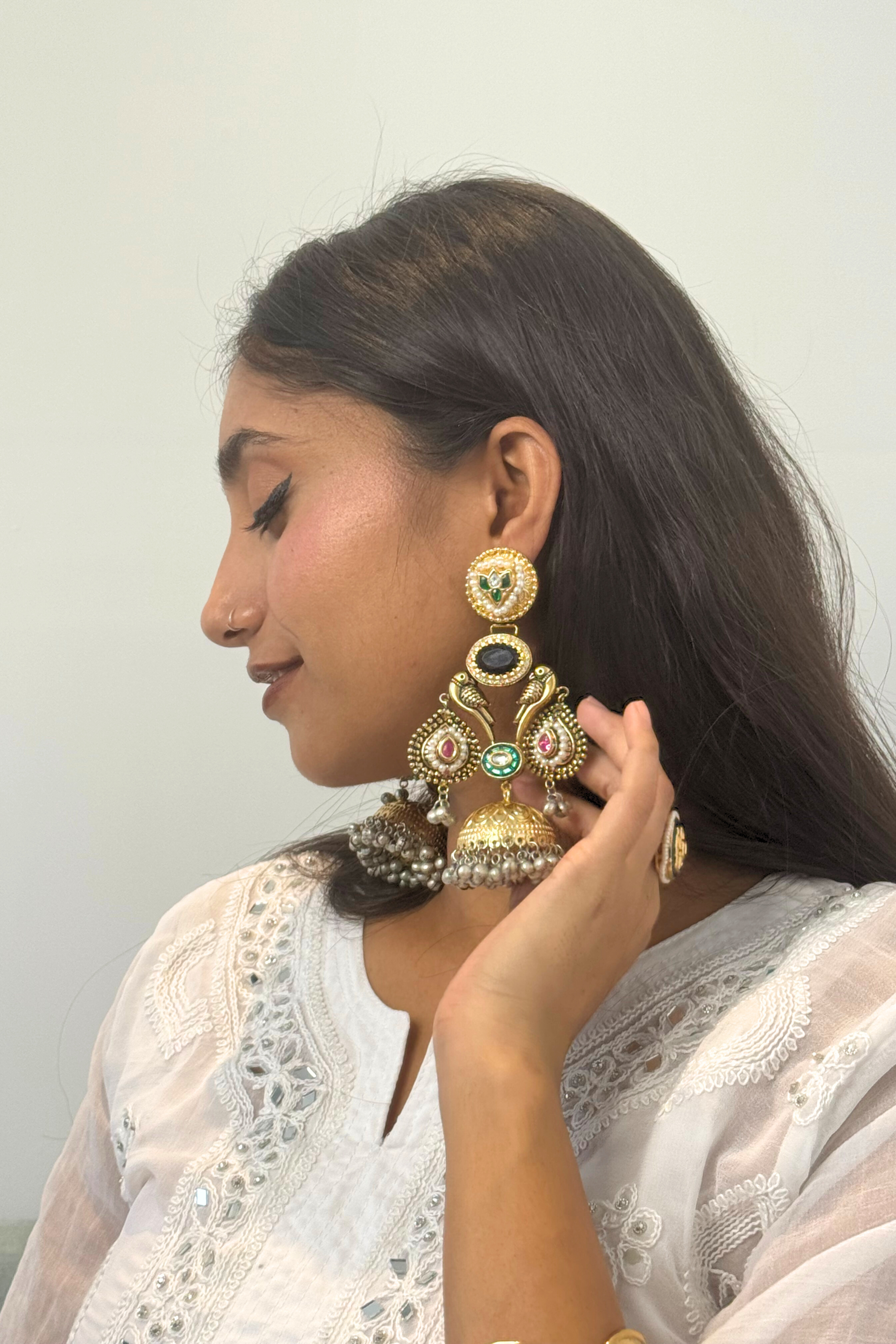 Woman wearing elaborate gold earrings with gemstones against a plain background
