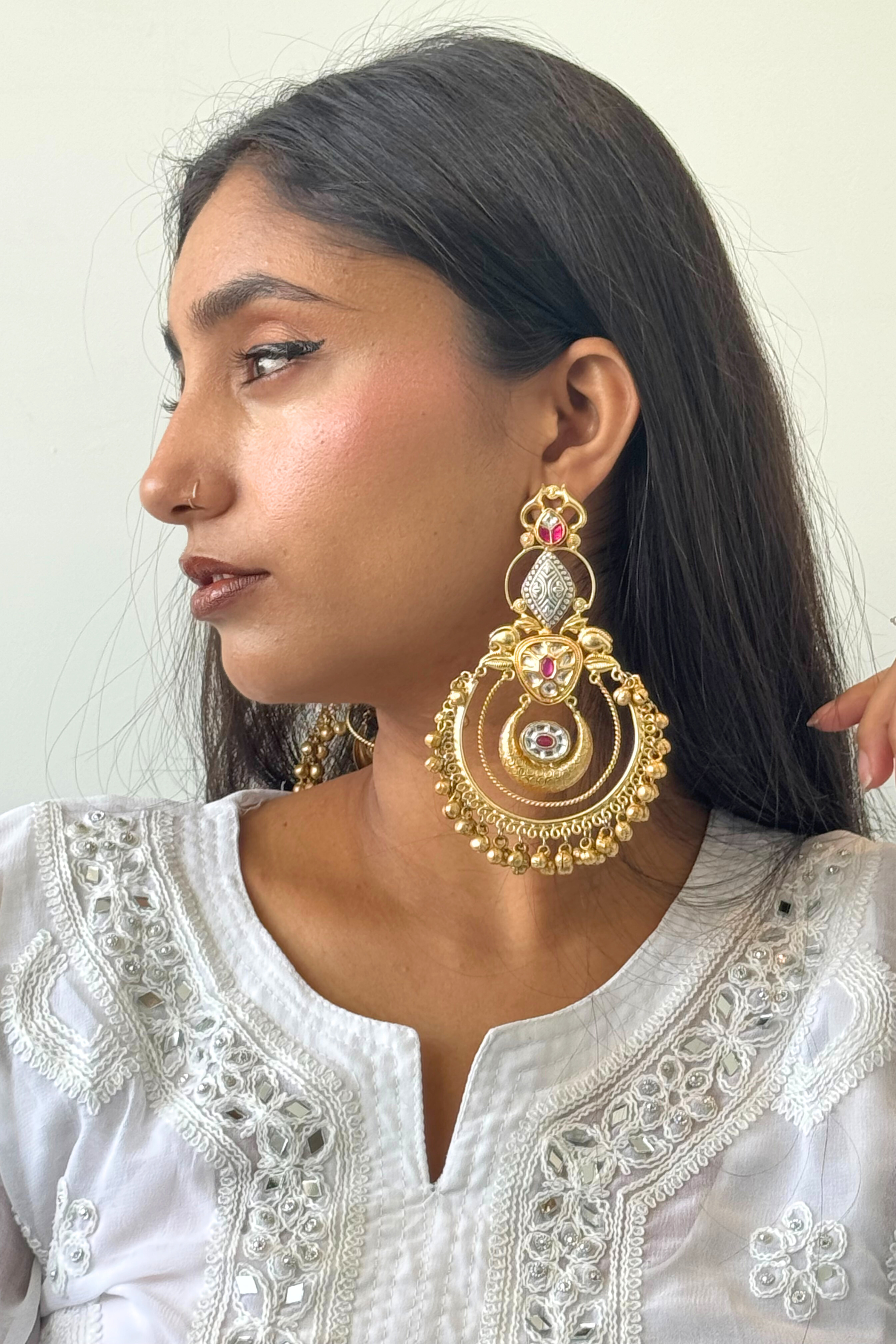 Woman wearing gold earrings with a white embroidered outfit