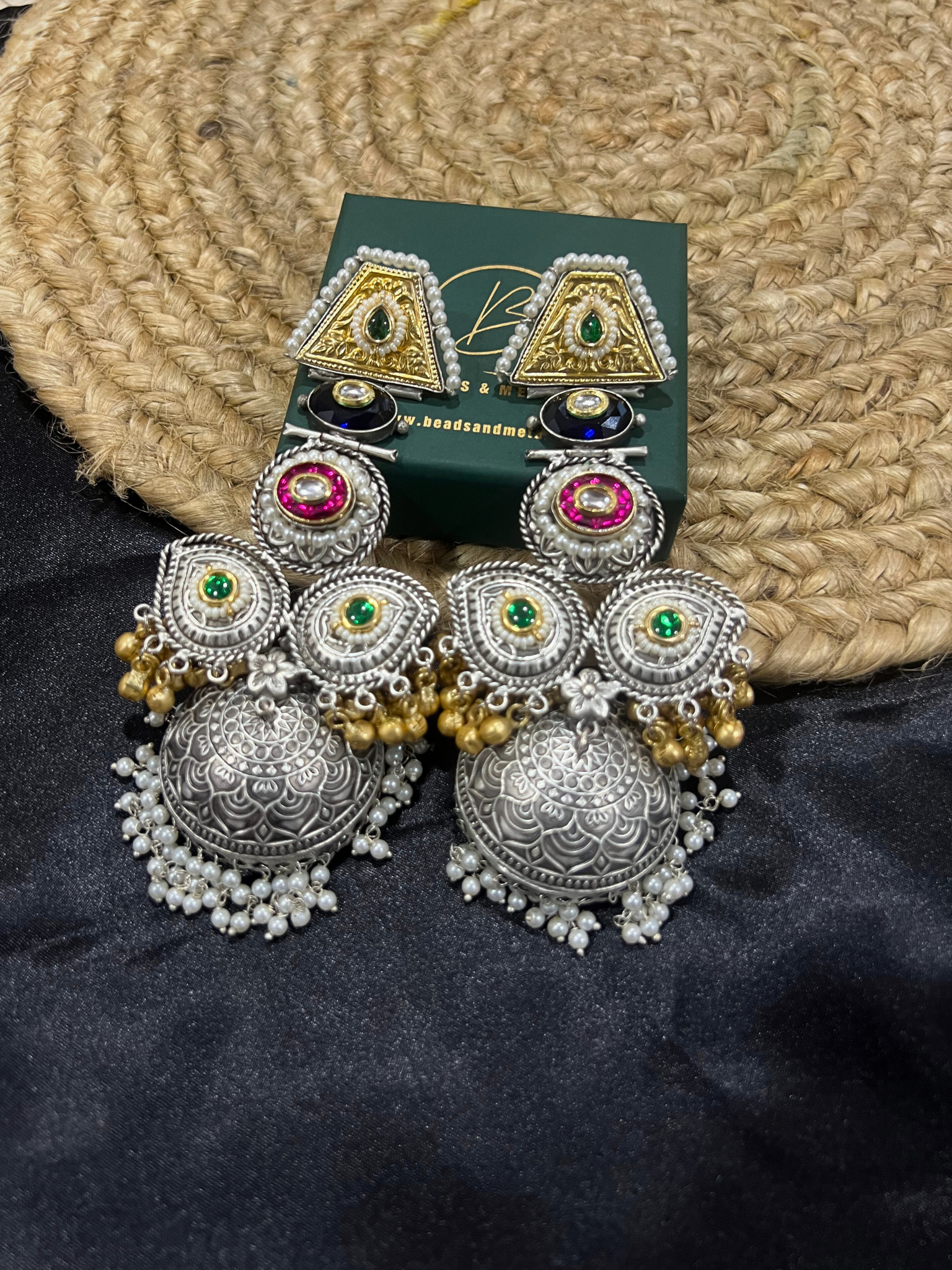 A pair of silver oxidised earrings for women with intricate designs and small pearls hanging, displayed against a dark background.